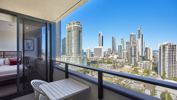 Ein Balkon mit Blick auf die Stadt, ein Bett sowie ein kleiner Tisch und ein Stuhl.