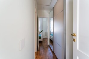 Een smalle gang met een houten vloer, witte muren en een deur met een gouden deurklink.