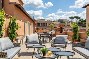 Eine Dachterrasse mit Sitzgelegenheiten im Freien, einem Esstisch und Blick auf die umliegenden Gebäude.