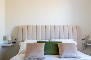 A neatly made bed with a padded headboard, two bedside tables with lamps, and a green and beige pillow arrangement.