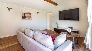 A modern living room with a sectional sofa, a round wooden coffee table, a flat-screen TV, and a dining area with a small table and chairs. - iFlat | Luxury Penthouse Piazza Venezia (Roma)