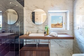 Ein modernes Badezimmer mit Marmorwaschtisch, zwei runden Spiegeln, einem Fenster mit Blick auf die Stadt und einer Dusche.