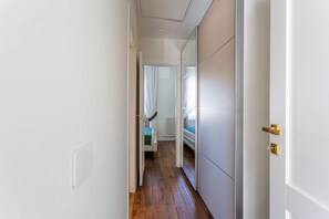 A narrow hallway with a wooden floor, white walls, and a door with a gold handle.