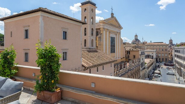 A building with a bell tower, a balcony with plants, and a street view. - iFlat | Luxury Penthouse Piazza Venezia (Roma)