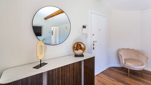 A room with a round mirror, a wooden number display, a decorative object, a white door, and a pink chair. - iFlat | Luxury Penthouse Piazza Venezia (Roma)