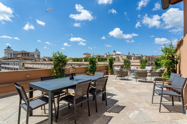 Eine Dachterrasse mit Tisch und Stühlen, Topfpflanzen und Blick auf historische Gebäude.