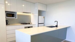 A modern kitchen with white cabinetry, a central island with a sink, a microwave, a stove, and a refrigerator.