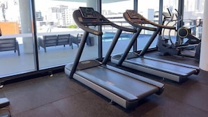 A gym with treadmills and exercise equipment, large windows with a city view, and a seating area with benches.