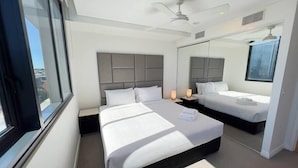 A modern hotel room with a large bed, a smaller bed, a ceiling fan, and a large mirror.