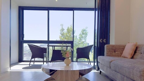 A modern living room with a round table, two chairs, a sofa, and a large window offering a view of greenery.