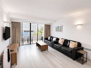 Ein modernes Wohnzimmer mit Sofa, Couchtisch, Fernseher und einem Balkon mit Vorhängen.