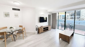 A modern living room with a dining area, a TV mounted on the wall, and a balcony with a city view. - Crown Towers Stunning 1Bedroom Apt 3-min to Beach (Surfers Paradise)