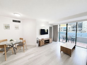 Ein modernes Wohnzimmer mit Essbereich, einem an der Wand montierten Fernseher und einem Balkon mit Blick auf die Stadt.