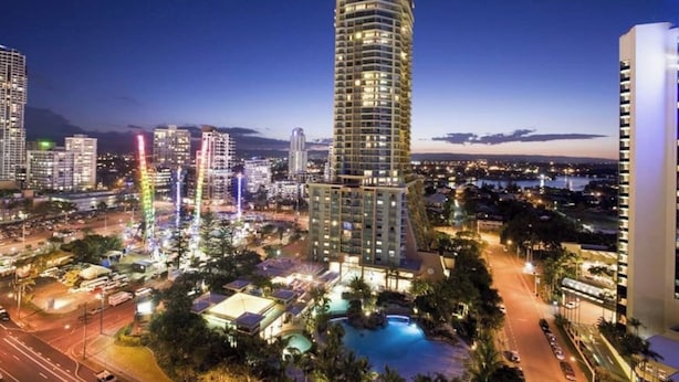 A high-rise hotel with a modern design, surrounded by a well-lit pool area and a cityscape at dusk. - Crown Towers Stunning 1Bedroom Apt 3-min to Beach (Surfers Paradise)