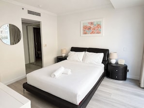 A modern hotel room with a large bed, two bedside tables, a mirror, and a painting on the wall.