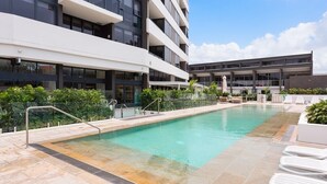 A modern building with a swimming pool, outdoor seating, and a clear sky. - Two Bedroom Apartment with view In SurfersParadise (Surfers Paradise)
