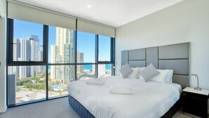 A modern hotel room with a large bed, a nightstand, and a view of the cityscape through floor-to-ceiling windows. - Two Bedroom Apartment with view In SurfersParadise (Surfers Paradise)