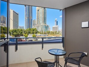Un balcón con vistas a un horizonte urbano, dos sillones de mimbre y una pequeña mesa redonda.