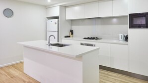 A modern kitchen with white cabinetry, a built-in island with a sink, a stove, and a microwave. - Cozy 2 Bedroom Apartment+study located in Surfers (Surfers Paradise)