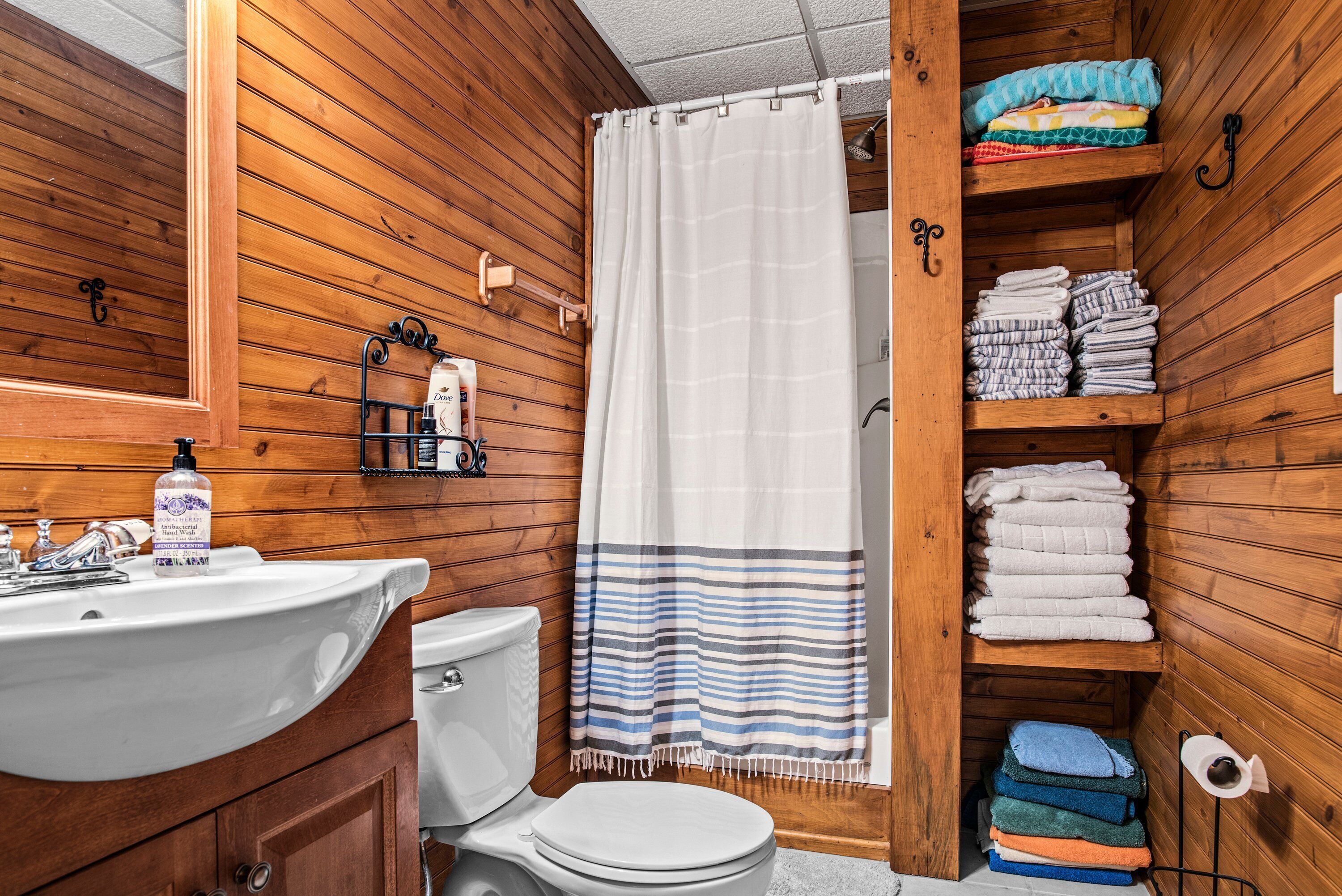 Een houten badkamer in een chalet, met een wit wastafel, toilet en douchegordijn.