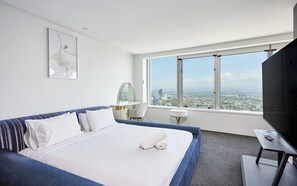 Quarto de hotel com uma cama grande, televisão, escrivaninha e vista para a paisagem urbana.
