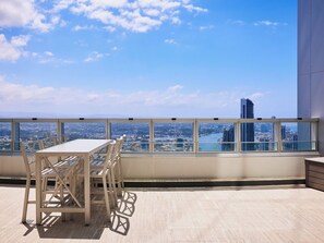 A high-rise balcony with a table and chairs, offering a cityscape view.
