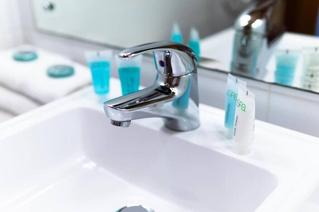 Une salle de bain moderne avec un robinet chromé, un lavabo blanc et un miroir qui reflète les articles de toilette.