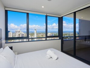 A hotel room with a large window offering a city view, a bed with white linens, and a glass door leading to a balcony. - Fantastic view 1 bedroom Apartment In Gold Coast (Surfers Paradise)