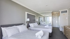 Habitación de hotel con tres camas, un aparador de madera y un baño con ducha e inodoro.