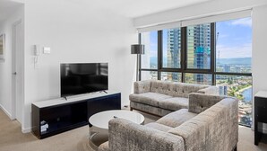 Una sala de estar moderna con un televisor de pantalla plana, un juego de sofá gris, una mesa de centro y un ventanal con vistas a la ciudad.