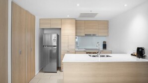 Una cocina moderna con un refrigerador de acero inoxidable, armarios de madera, una encimera blanca y un hervidor eléctrico negro.
