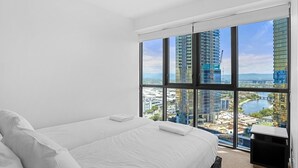 Habitación de hotel moderna con una cama grande, televisión y vistas de un paisaje urbano a través de ventanales.