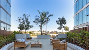 Una terraza en la azotea con mobiliario de madera, palmeras y vistas a edificios.