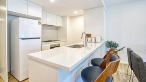 Una cocina moderna con armarios blancos, horno integrado, un lavamanos y un pequeño comedor con dos sillas.