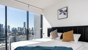 Ett modernt hotellrum med en stor säng, utsikt över staden, en svart sänggavel och ett inramat konstverk på väggen.