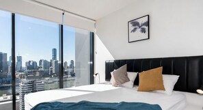 Un hotel moderno con una cama grande, vistas a la ciudad y una obra enmarcada en la pared.