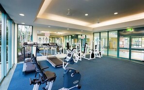 Une salle de sport équipée de tapis de course, d’appareils de musculation et recouverte d’une moquette bleue.