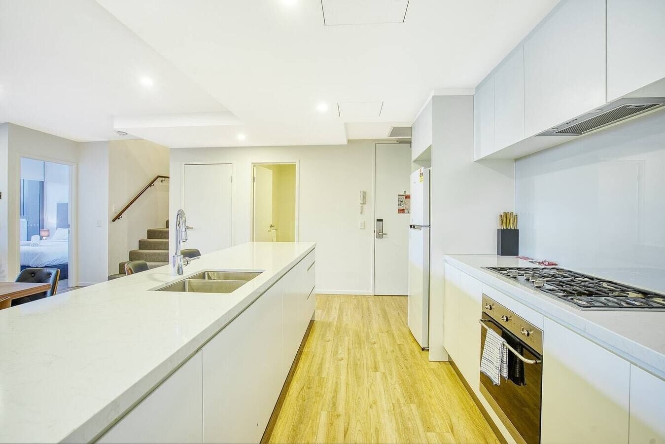 A modern kitchen with white cabinetry, a central island with a sink, a stove, and a refrigerator.