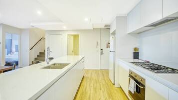 A modern kitchen with white cabinetry, a central island with a sink, a stove, and a refrigerator.