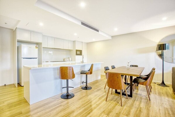 A modern kitchen with white cabinets, a central island with stools, and a dining area with a wooden table and chairs.