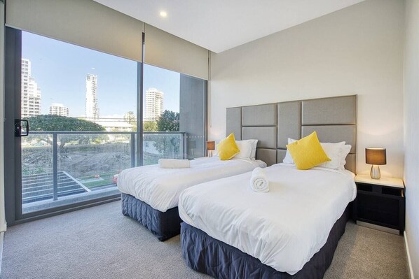 A modern hotel room with two beds, large windows, and a city view.