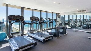 Un gimnasio moderno con cintas de correr, elípticas y pelotas de ejercicio, con amplios ventanales que ofrecen vistas a la ciudad.