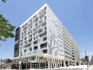 Un immeuble moderne à plusieurs étages, doté d’une façade remarquable ornée d’un motif représentant un arbre.