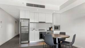 A modern kitchen with white cabinets, a stainless steel refrigerator, a microwave, and a dining area with a round table and four chairs.
