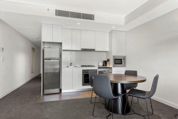 Een moderne keuken met witte kasten, een roestvrijstalen koelkast, een magnetron, en een eethoek met een ronde tafel en vier stoelen.