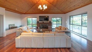A spacious living room with a large sectional sofa, a fireplace, and large windows offering views of the outdoors. - The Hideaway by Gatt Wines (Flaxman Valley)