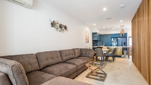 Ein modernes Wohnzimmer mit einer Eckcouch, einem Couchtisch und einem Essbereich mit Stühlen sowie einer Küche im Hintergrund.