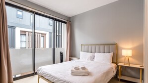 Ein Hotelzimmer mit einem großen Bett, einem Nachttisch mit Lampe und Blick durch eine Schiebetür.