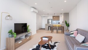 Un salon moderne doté d’un téléviseur à écran plat, d’un meuble de rangement en bois et d’un canapé agrémenté de coussins décoratifs.