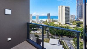 A balcony with a view of the ocean and cityscape, including tall buildings and a construction crane. - Stylish 1 Bedroom + Partial Ocean View In Surfers (Surfers Paradise)